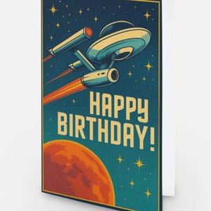 May include: A rectangular greeting card featuring a space-themed illustration of a starship flying past a large orange planet against a dark blue starry sky. The text HAPPY BIRTHDAY! is printed in large, bold, light yellow capital letters.