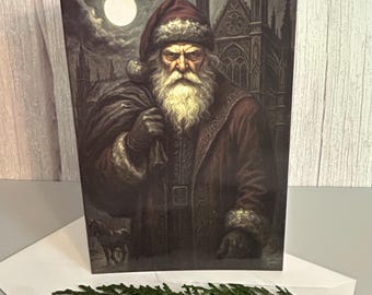 May include: A rectangular greeting card featuring a dark, atmospheric illustration of a bearded figure in a fur-trimmed red coat and hat, carrying a sack. The background shows a gothic building under a full moon and a small horse silhouette.