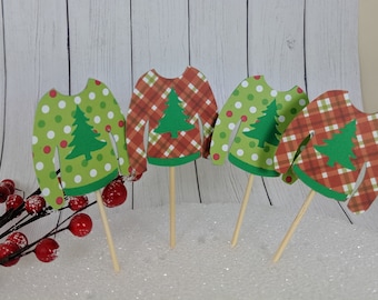 May include: Four festive Christmas sweater cupcake toppers. Each topper features a different design: green with white polka dots, red and green plaid, green with white polka dots, and red and green plaid. Each topper has a green Christmas tree in the center.