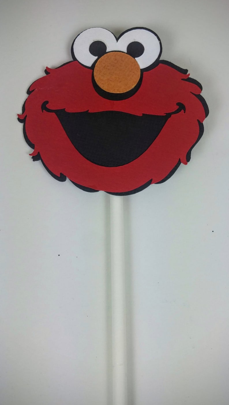 K&ouml;nnte beinhalten: Roter Filz-Elmo-Charakter-Gesichtsausschnitt auf einem wei&szlig;en Stiel. Der Charakter hat gro&szlig;e wei&szlig;e Augen, einen schwarzen Mund und eine rote Nase.