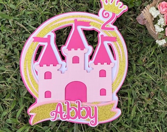Topo de bolo personalizado com castelo de princesa, nome em rosa e dourado com glitter.