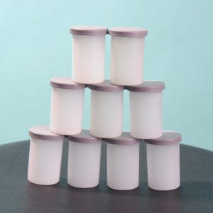 May include: A stack of eight white film canisters with purple lids. The canisters are arranged in a pyramid shape.