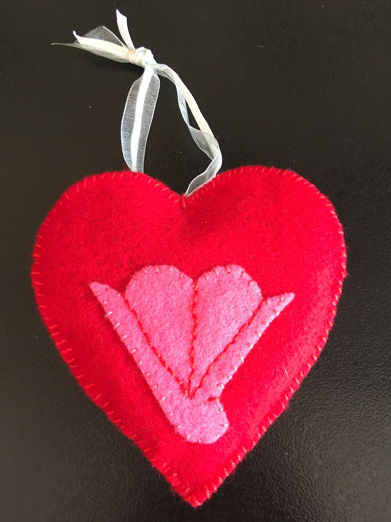 May include: A red felt heart with a pink felt flower in the center. The heart has a white ribbon attached to the top.