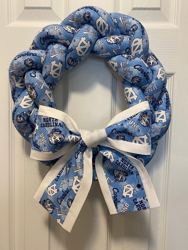 K&ouml;nnte beinhalten: Ein blauer und wei&szlig;er Kranz mit Schleife. Der Kranz ist aus Stoff und zeigt das UNC Tar Heels Logo und die Worte "North Carolina".