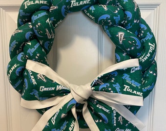 May include: A green and blue wreath with a white bow. The wreath is made of fabric and has the words "Tulane Green Wave" printed on it.