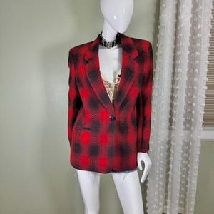 May include: A red and black plaid blazer with a single-button closure. The blazer has a classic notched lapel and two front pockets. The fabric appears to be a wool blend. The blazer is displayed on a mannequin.