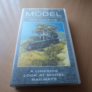 Pode incluir: Uma fita de vídeo VHS com um rótulo azul e branco. O rótulo diz "Model Railways" e "A Lineside Look at Model Railways". A imagem da capa mostra um trem modelo em uma paisagem verde.