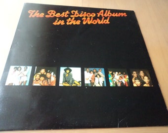 May include: A black vinyl record album cover with the text "The Best Disco Album in the World" in orange lettering. The cover features eight small photos of different disco music artists.