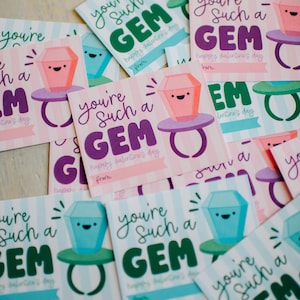 May include: Valentine's Day cards with a gem ring design. The cards display the text "you're such a GEM" in colours like pink, green, and purple. Each card has a cartoon gem ring illustration, perfect for a loved one.