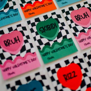 May include: A set of ten Valentine's Day cards featuring different slang words printed on heart-shaped candy designs. The cards have a black and white checkered background and the words "Happy Valentine's Day" and "From:" are printed on each card.