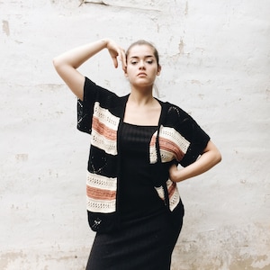 Puede incluir: Una mujer con un cárdigan de crochet a rayas blancas y negras con un vestido negro debajo. El cárdigan tiene una raya rosa.