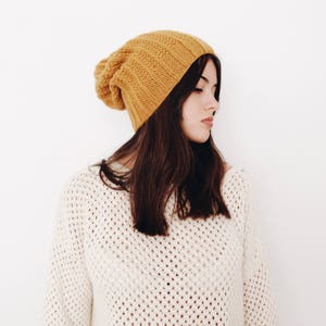 May include: A woman wearing a mustard yellow knitted beanie and a white crocheted sweater.