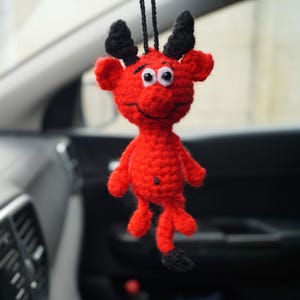 Pode incluir: Uma pequena figura de crochê feita à mão de um diabo vermelho com chifres pretos e uma cauda com ponta preta. O personagem tem dois olhos de plástico branco com pupilas pretas, um sorriso bordado e um cordão preto para pendurar.