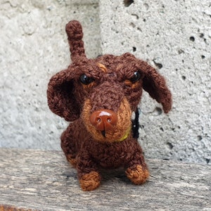 May include: A brown and tan crocheted dachshund dog toy with black eyes and a brown nose.