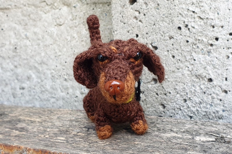 May include: A brown and tan crocheted dachshund dog toy with black eyes and a brown nose.