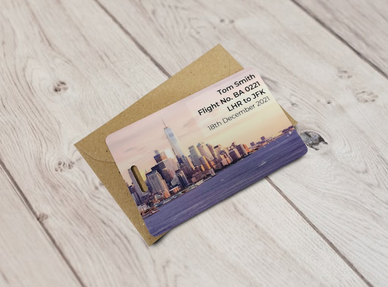 May include: A luggage tag featuring a cityscape of New York City at sunset. The tag has the text "Tom Smith, Flight No. BA 0221, LHR to JFK, 18th December 2021" printed on it.