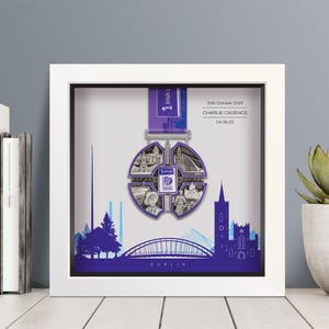 Könnte beinhalten: Gerahmte Gedenkmedaille vom 1 Life Run 2025 in Dublin, Irland. Die silberfarbene Medaille zeigt Dubliner Wahrzeichen. Der weiße Rahmen umgibt eine violette Silhouette der Stadt. Der Text auf dem Rahmen lautet "26. Oktober 2025, Charlie Cadence, 04:26:25."