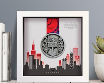 Puede incluir: Un marco blanco tipo caja que contiene una medalla de finalista del Maratón de Chicago 2025 suspendida por una cinta roja y azul. El fondo presenta un gráfico del horizonte de Chicago en negro y rojo con el texto October 12th, 2025, CHARLIE CADENCE, 04:12:25.