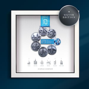 Puede incluir: Medallas de maratón plateadas enmarcadas, con paisajes urbanos de Tokio, Boston, Londres, Berlín, Chicago y Nueva York. Las medallas están dispuestas en un patrón circular, con una cinta azul y el texto "Silver Edition". El marco es blanco.