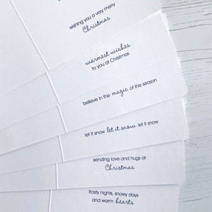 May include: A stack of white Christmas cards with various holiday greetings printed in dark blue ink. The messages include "wishing you a very merry Christmas" and "warmest wishes to you at Christmas."