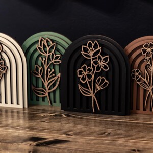 May include: Four wooden arch-shaped wall decor pieces with a floral design. The arches are in white, green, black, and brown.