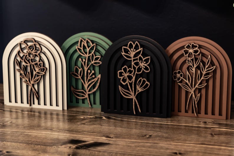 May include: Four wooden arch-shaped wall decor pieces with a floral design. The arches are in white, green, black, and brown.