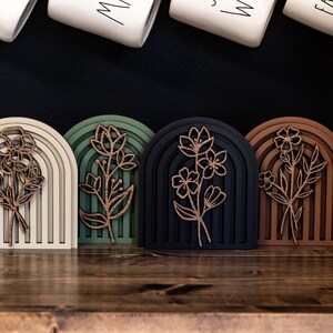 May include: Four wooden rainbow arches with a floral design in the centre. The arches are in different colours: beige, green, black, and brown.