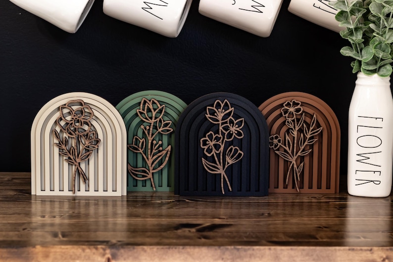 May include: Four wooden rainbow arches with a floral design in the centre. The arches are in different colours: beige, green, black, and brown.