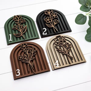 May include: Four wooden wall decorations featuring a floral design and a rainbow arch. The pieces are in different colours: green, black, brown, and beige. The numbers 1, 2, 3, and 4 are written on the pieces.
