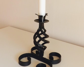 May include: Black metal candle holder with a spiral design and a white candle. The holder has a three-pronged base.
