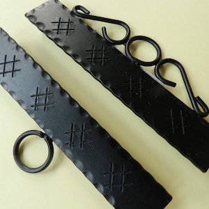 Könnte beinhalten: Zwei schwarze Metallhaken mit einem dekorativen Kreuzmuster. Ein Haken hat einen Ring am Ende und der andere einen gebogenen Haken.