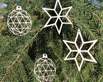 Op de afbeelding: Witte geometrische kerstversieringen, waaronder twee sterren en twee bolvormige vormen, hangen aan een groene kerstboom. De ornamenten hebben een modern, minimalistisch ontwerp.