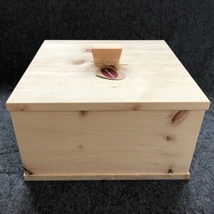 Op de afbeelding: Een natuurlijke houten doos met een scharnierend deksel en een kleine houten knop bovenop. De doos is gemaakt van licht hout en heeft een natuurlijke afwerking. De doos is gelabeld met "remarkable".