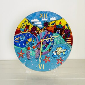 Könnte beinhalten: Eine skurrile Uhr mit einer blauen Katze, einem Fisch und einem Schloss auf blauem Hintergrund. Das Zifferblatt der Uhr hat römische Ziffern und goldene Zeiger.