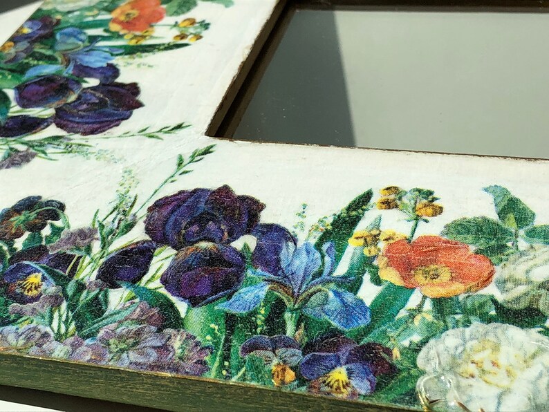 May include: A white wooden picture frame with a floral design. The frame is decorated with a collage of colorful flowers, including purple irises, pansies, and orange poppies. The frame has a distressed, vintage look.