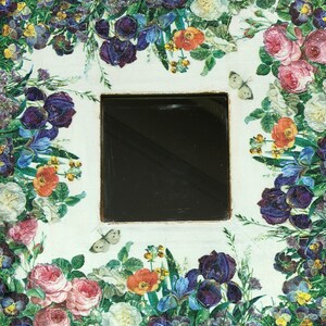 May include: Square decorative item with a black center, surrounded by a floral design. The flowers include roses, irises, and pansies in shades of pink, purple, orange, and white. Two butterflies are also present.