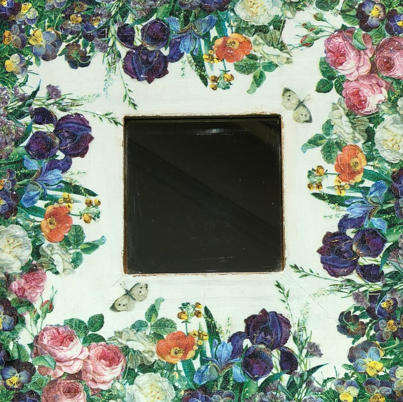 May include: Square decorative item with a black center, surrounded by a floral design. The flowers include roses, irises, and pansies in shades of pink, purple, orange, and white. Two butterflies are also present.