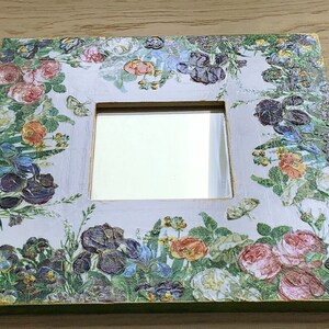 May include: Square decorative mirror with a floral design. The frame is white with a green edge and is covered in a pattern of colorful flowers, including roses, irises, and pansies. Butterflies are also featured in the design.