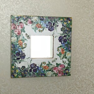 May include: Square decorative mirror with a floral design. The frame is white with a collage of colorful flowers, including roses and irises, and butterflies. The mirror is square and has a gold trim.