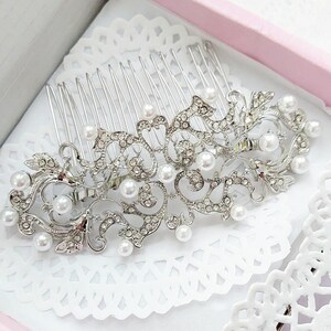May include: Silver hair comb with a pearl and rhinestone design. The comb has a delicate, ornate pattern with a floral motif.