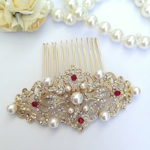 May include: Gold hair comb with a pearl and rhinestone design. The comb has a decorative filigree pattern with red gemstones.