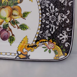 Puede incluir: Plato rectangular de cer&aacute;mica con fondo blanco y dise&ntilde;o pintado de frutas y flores. El dise&ntilde;o incluye manzanas amarillas, cerezas rojas y ciruelas moradas. El borde presenta un patr&oacute;n floral en blanco y negro con detalles dorados.