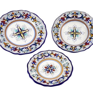 May include: Three white ceramic plates with scalloped edges and intricate floral designs. The plates feature a blue border, a central floral motif, and accents of yellow, red, and green. The plates vary in size.