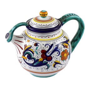 May include: A white ceramic teapot with a green handle and lid. The teapot is decorated with a colourful floral pattern in shades of blue, green, yellow, orange, and red.