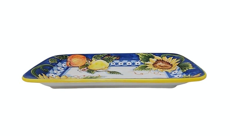 May include: Rectangular ceramic serving platter with a hand-painted design. The platter features a blue border with fruit and sunflower motifs. The rim is yellow, and the center is white.