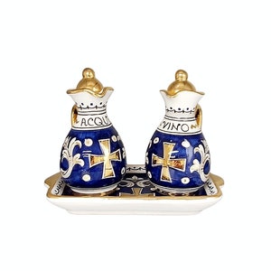 Puede incluir: Dos jarras de cerámica azul y dorada con tapas, etiquetadas "ACQUA" y "VINO", sobre una bandeja blanca con ribete dorado.