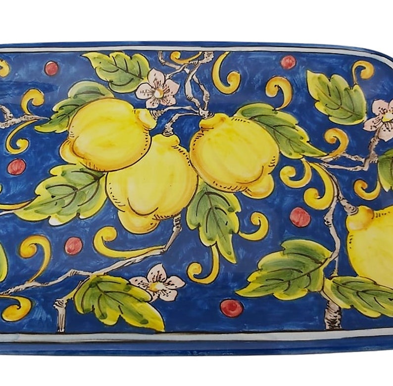 May include: Rectangular ceramic serving platter with a hand-painted design. The platter features a deep blue background with yellow lemons, green leaves, and delicate white flowers. The edges are outlined in white.