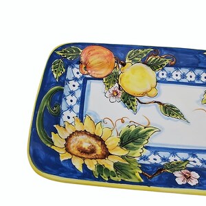 May include: Rectangular ceramic serving platter with a vibrant fruit and floral design. The border is a deep blue with a yellow edge. The center features a sunflower, peaches, lemons, and delicate pink flowers.