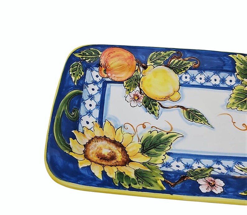May include: Rectangular ceramic serving platter with a vibrant fruit and floral design. The border is a deep blue with a yellow edge. The center features a sunflower, peaches, lemons, and delicate pink flowers.