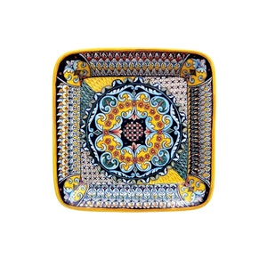 May include: A square ceramic serving dish with a yellow background and intricate blue, green, and red floral patterns. The dish has a raised rim and a decorative border.